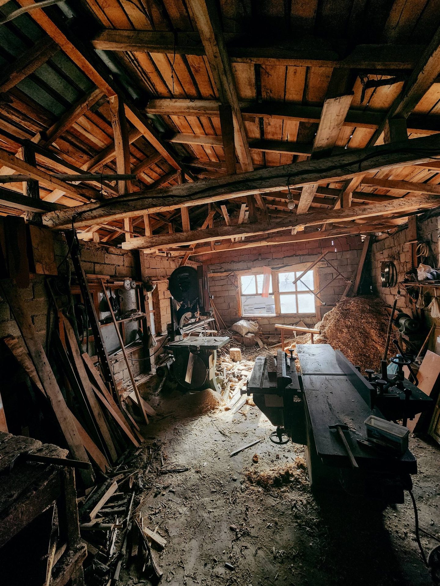 Blick in eine Holzwerkstatt mit gelagertem Holz und Werkzeug.